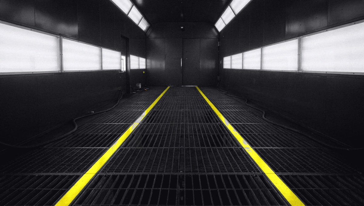 Downdraft spray booth interior, lit wall panels and hi-vis floor lines receding to the far doors